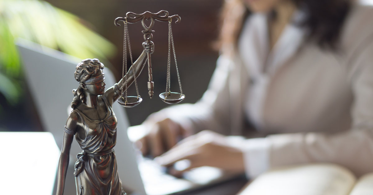Tailored Law Firm Website - Scales of Justice figure in the foreground and an attorney using her laptop in the background.